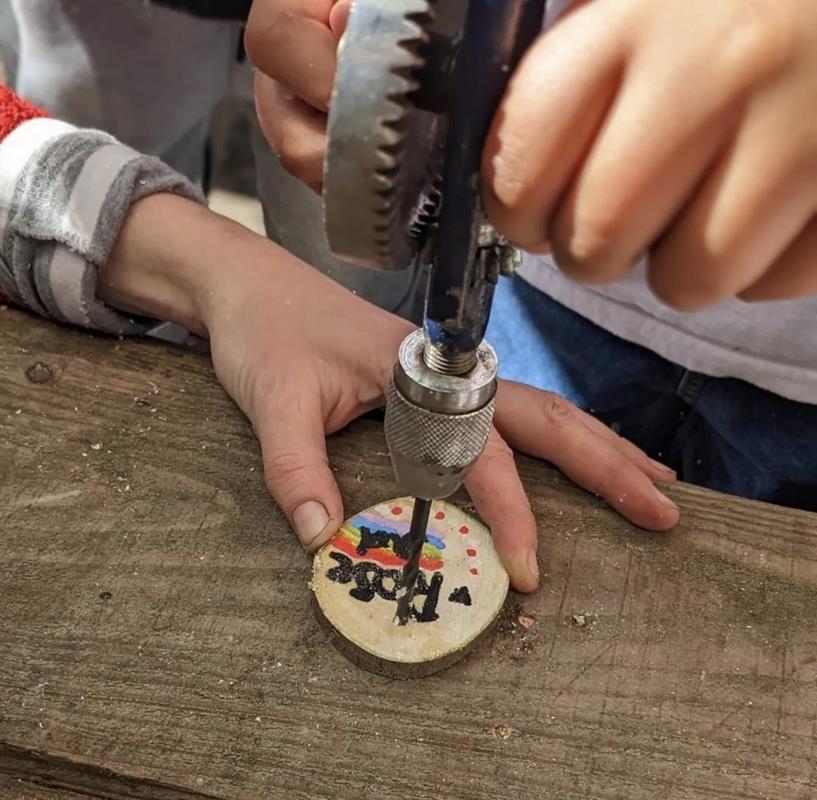 Children learning woodcraft, drilling a decorated disc of wood.