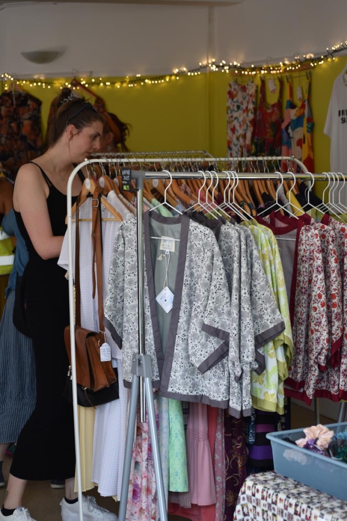 Woman looking through a clothes rail of silky kimono tops at a market stall