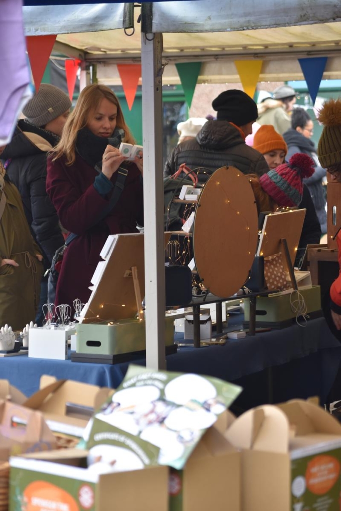 Customers browsing hand-made jewellery at a Christmas market stall.